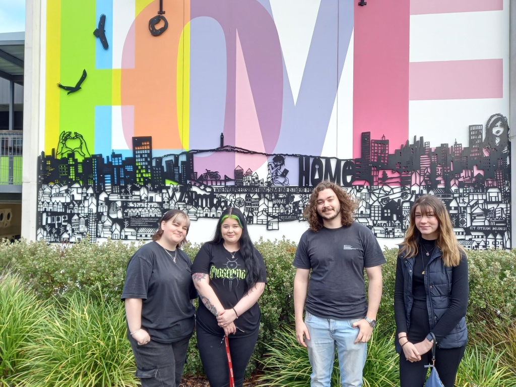 Four young Tasmanians enrolled in the Youth 2 Independence program stand in front of a sign that says 'Home'.